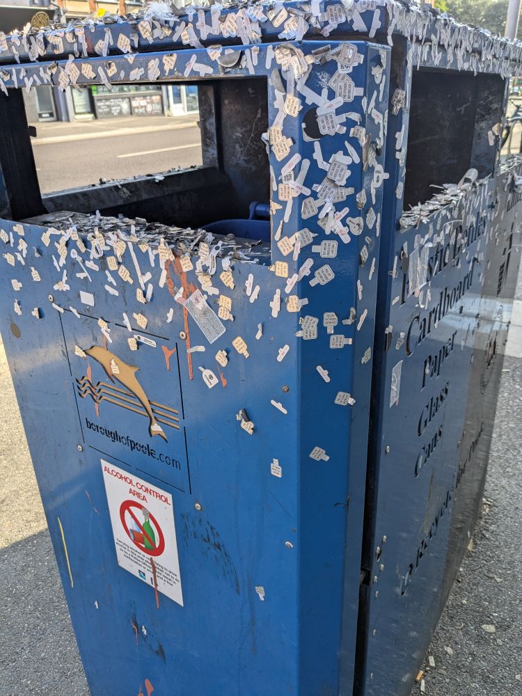 A public litter bin covered with little stickers from vapes.