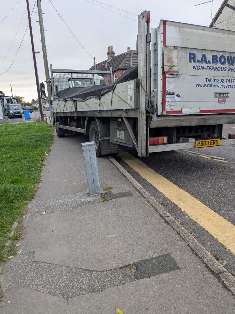 Photo of a scrap metal truck parked diagonally across the footway and partially blocking a bus stop layby.