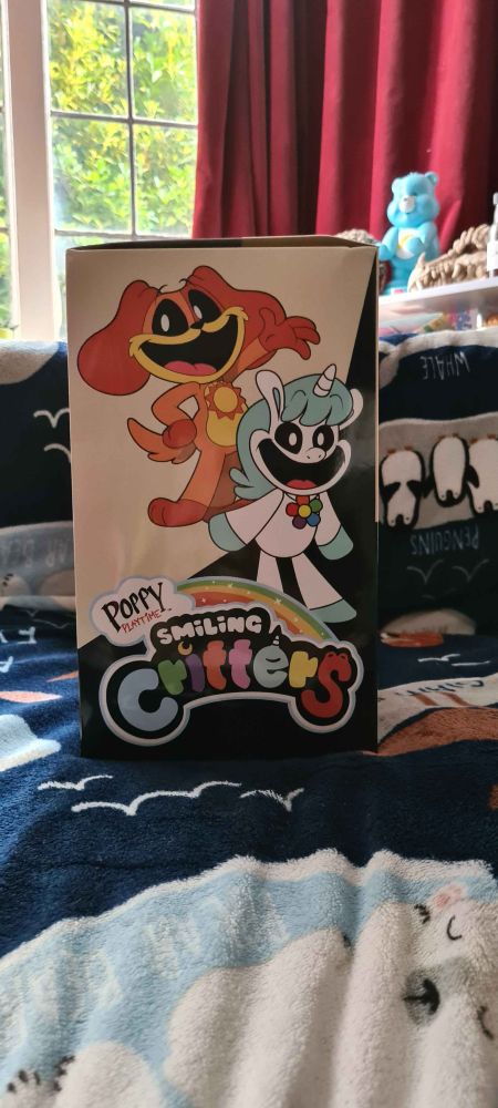 side of box, it has the Smiling Critters logo and pictures of an orange dog (DogDay) and a white and blue unicorn (CraftyCorn)