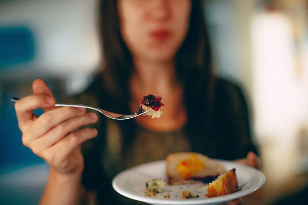 Lady with a piece of cake on a fork offering it towards the camera