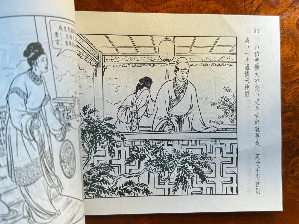Una página del lianhuanhua. La ilustración, en tinta negra y de trazo fino, muestra a los protagonistas en un quiosco exterior rodeado de arbustos y vegetación. Él acaba de enterarse de que han prometido su amada a otro hombre y está muy disgustado; se ha puesto de pie para apoyarse en la barandilla, sobre la que posa el puño derecho. Ella, a su espalda, se tapa la cara con la manga, pero parece que quiere acercársele. A la derecha de la ilustración hay un texto explicativo que dice algo así como «Abrumado por la pena, Liang Shanbo se levanta dispuesto a marcharse, pero un gesto de afecto lo detiene: Zhu Yungtai se opone a su partida».