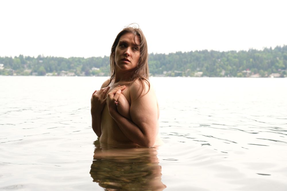 Olivia skinnydipping in a lake on a cloudy day, halfway submerged in the water