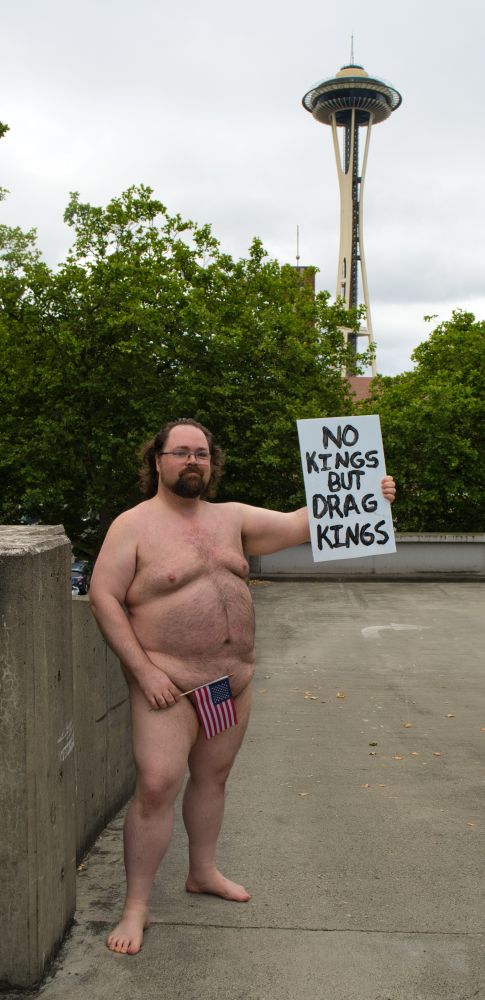 Nathaniel standing nude in front of the Seattle Space Needle holding a sign that says 'No kings but drag kings,' and an American flag.

Thanks to @lezsmokehoney.bsky.social for taking this photo of me!