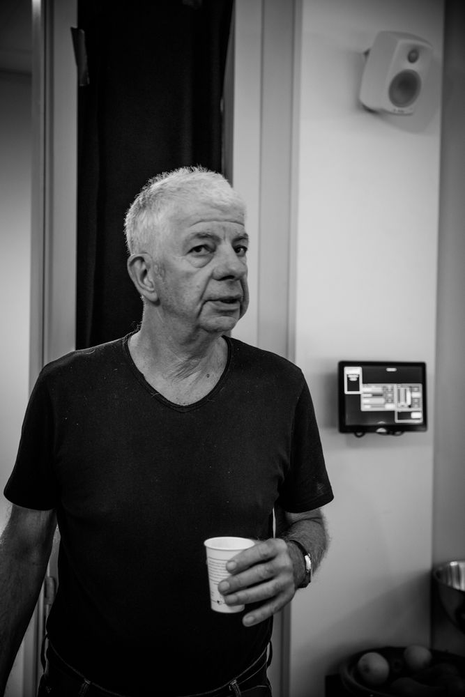 Black and white photo of a person with gray hair holding a cup of coffee and looking into the camera.