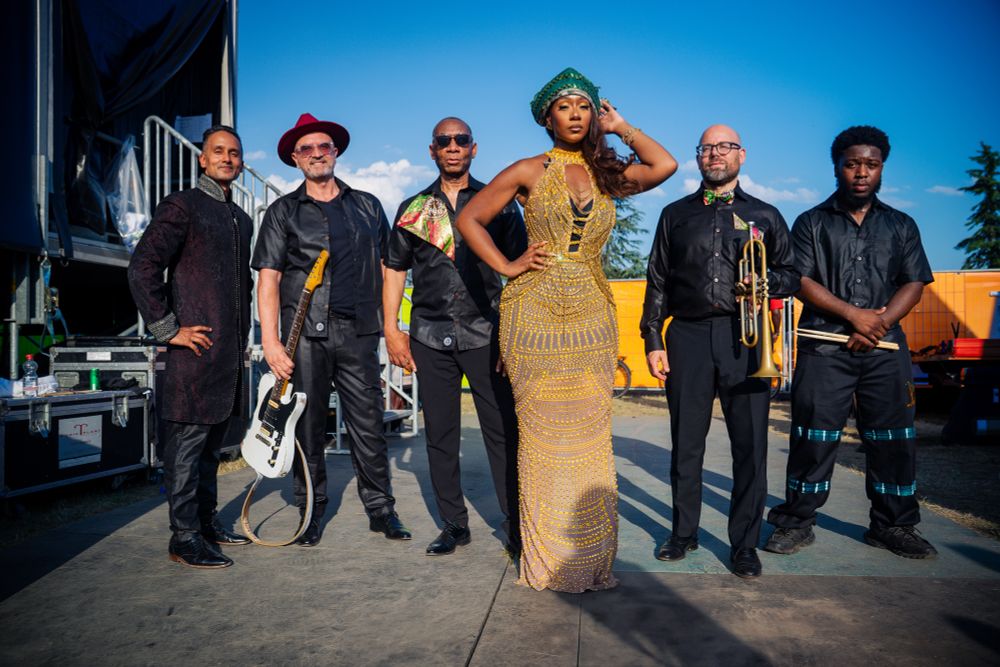 Five musicians posing backstage in concert clothing.