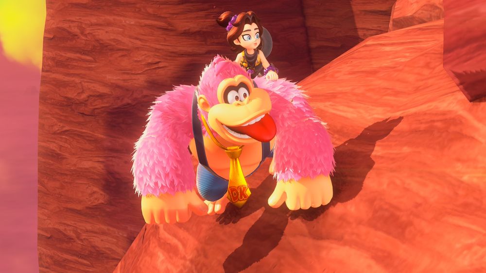 Donkey Kong with pink fun and a golden tie with the DK logo in red.  He grins goofily with his tongue out at something off-screen.  Pauline rides on his back, her cowboy hat hanging off the back of her head.