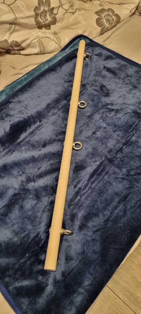 Beschreibung von chatgpt: Das Foto zeigt ein längliches, helles Holzstück, das auf einer dunkelblauen, samtähnlichen Decke liegt. Am Holzstück sind mehrere Metallringe befestigt, die gleichmäßig entlang seiner Länge angebracht sind. Im Hintergrund ist ein Bett mit einer beige-gemusterten Bettdecke zu erkennen. Die Szene wirkt ordentlich arrangiert, möglicherweise handelt es sich um ein handwerkliches oder dekoratives Objekt.