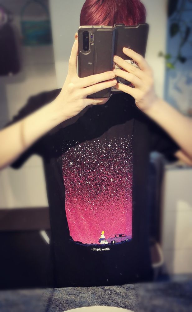 Thin guy wearing a shirt with a printed homer simpson, sitting on his car, looking into the night sky and says "stupid world"