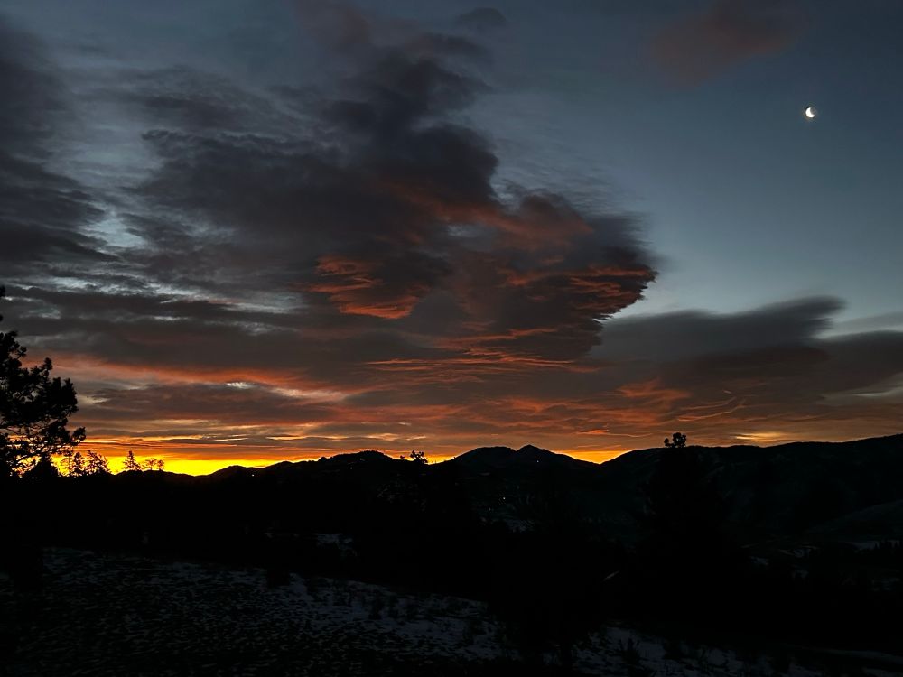 Impressive cloud formation at dawn with deep orange colors beneath the gray.  Partial moon in looking down from above.