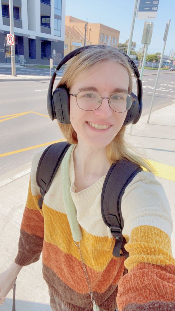 Cute dork standing outside in a autumn-coloured sweater wearing headphones.