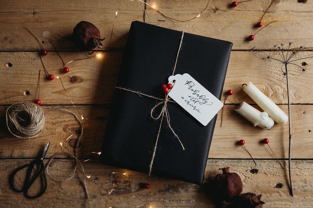 A photo of a present wrapped in black paper with a twine, red berries and a white tag. 'Probably not a mimic' is written on the tag in black calligraphy.