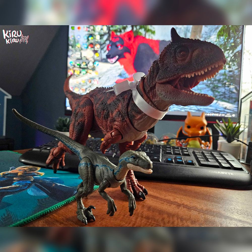 2 toy dinosaurs in running poses.
The scene takes place on a desk, you can see a keyboard and a screen among other things