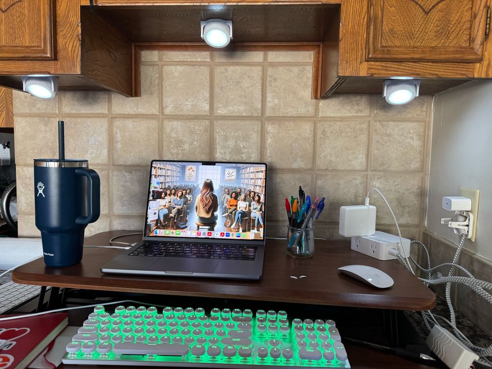Laptop with image of woman in front of a small crowd, backlit keyboard and workspace