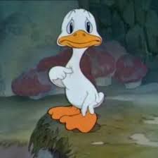 Meme do patinho branco, sobre um gramado, diante de alguns cogumelos foscos, apontando a patinha para si mesmo e deixando subentendida a pergunta “eu?”