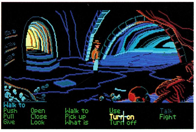 An early screenshot of Indiana Jones and the Last Crusade adventure game, from Game Player's PC Strategy Guide vol. 2 #4, September/October 1989. Indy is standing in the catacombs, by the hatch leading up from the room where he can find inscriptions talking about the Grail. Indy is facing right, but his sprite is a mirrored version of that in the previous screenshot, meaning he is now holding his whip in his left hand. The "Fight" verb is still in the GUI and apparently active  in place of "Travel".
