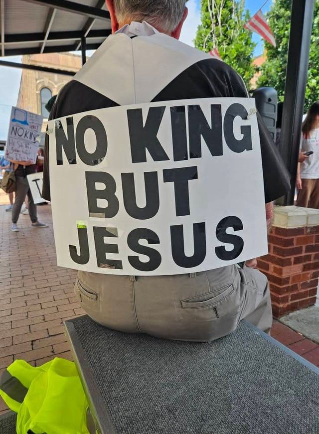 A sign trashed to the back of a serrated protestor at a No Kings protest reads, in big block letters, “NO KING BUT JESUS.”