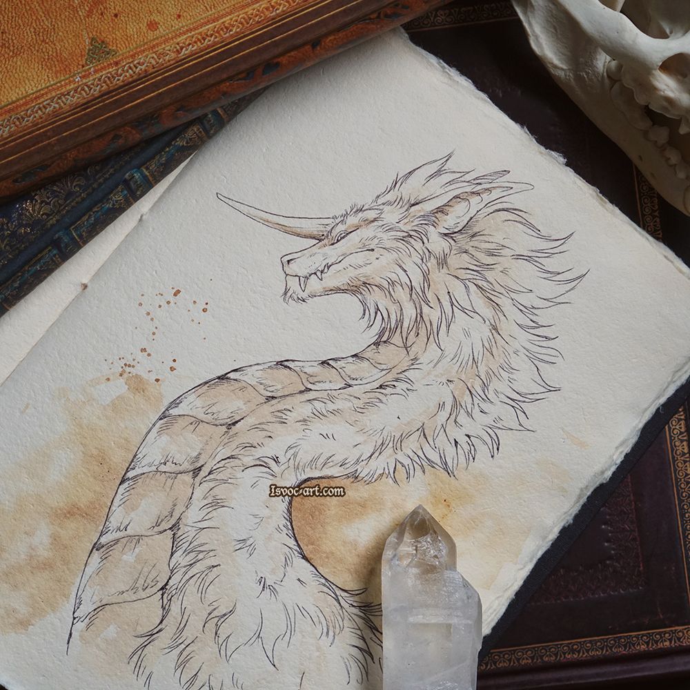 Photo of a sketchbook with a drawing of a dragon's portrait. It is fluffy, serpentine and has a forward facing horn.