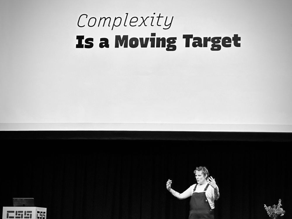 Mia on stage with a text-only slide: 

Complexity
Is a Moving Target