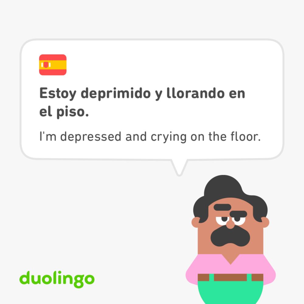 Screenshot from Duolingo showing a speech bubble that says in Spanish and then in English, “I’m depressed and crying on the floor.” The illustrated character in the bottom right of the image has brown skin, dark hair, and a mustache. He is wearing a pink shirt and green pants with a brown belt.