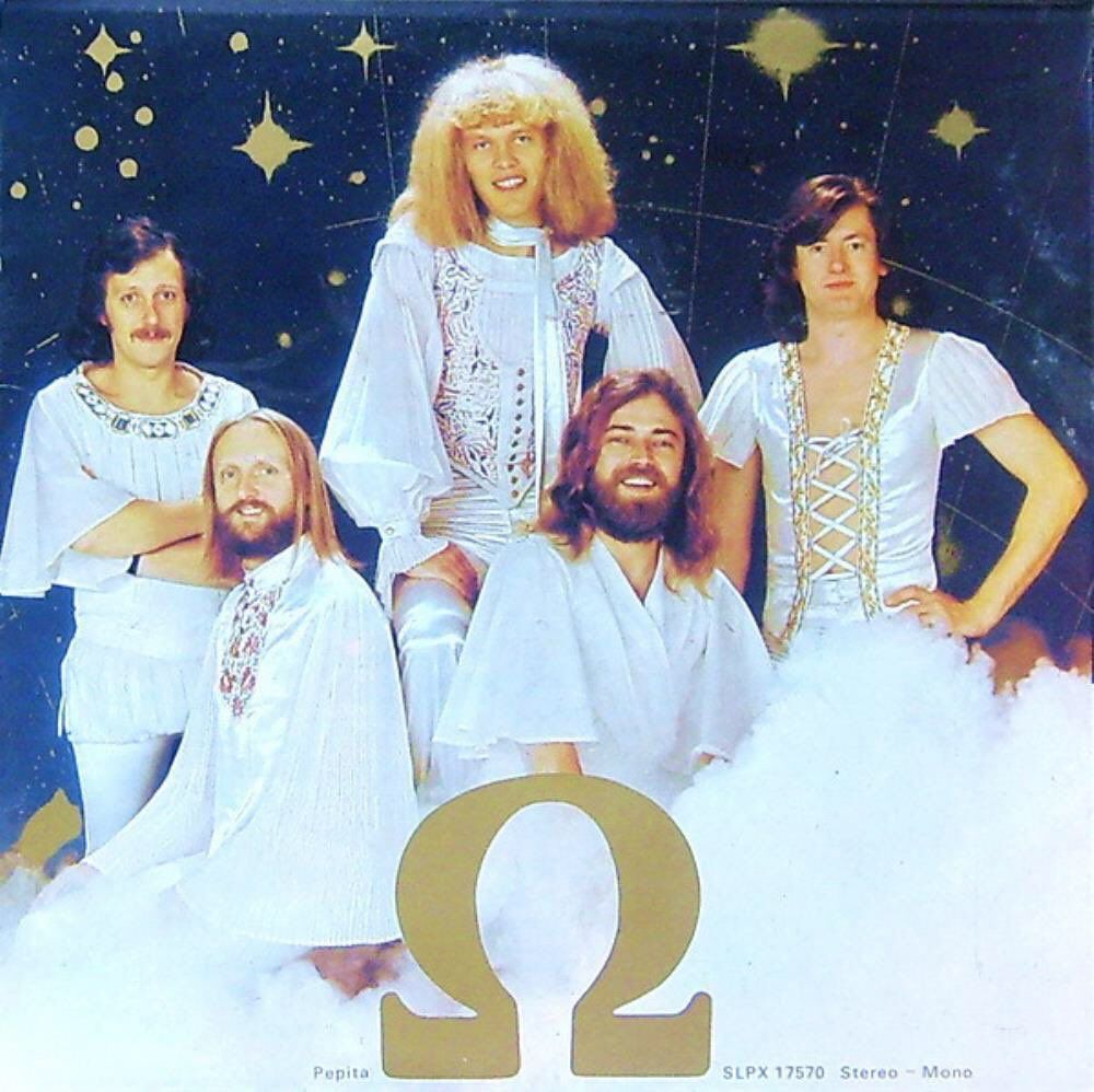 The various members of the band, two sitting, three standing, face the camera. They’re wearing a variety of white, flowing outfits. Laced-up panels are happening.

Hairstyles. Oh gods, the hairstyles. A mixture of Space Bee-Gee, Jimmy Page in drag, and Lenny the Lion.

Quite the mixture.