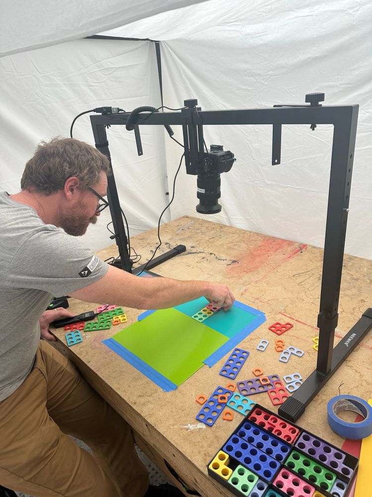 A guy is placing blocks on a mat with a camera on a rig pointing down to capture the image for animation. 