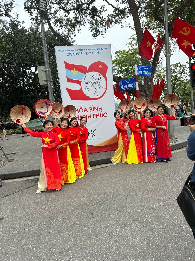 Women in red ao dai pose beneath a poster celebrating the 50th anniversary of Vietnamese reunification