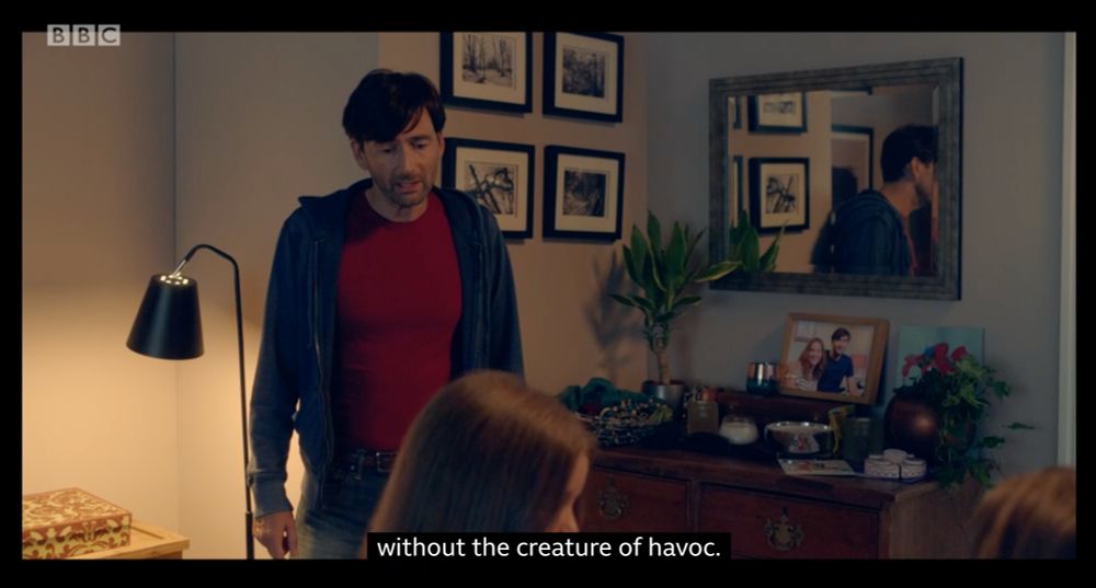 A screencap from the TV show There She Goes, series 1 episode 1. Simon Yates is talking to his wife Rosie Ann Yates, with the subtitles reading, "without the creature of havoc" - a possible reference to the twenty-fourth Fighting Fantasy gamebook, Creature of Havoc.