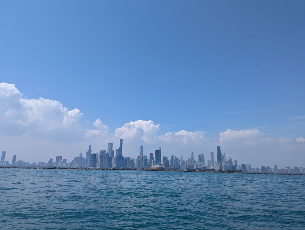 The Chicago city skyline taken from lake Michigan, backed by low clouds and a blue sky.