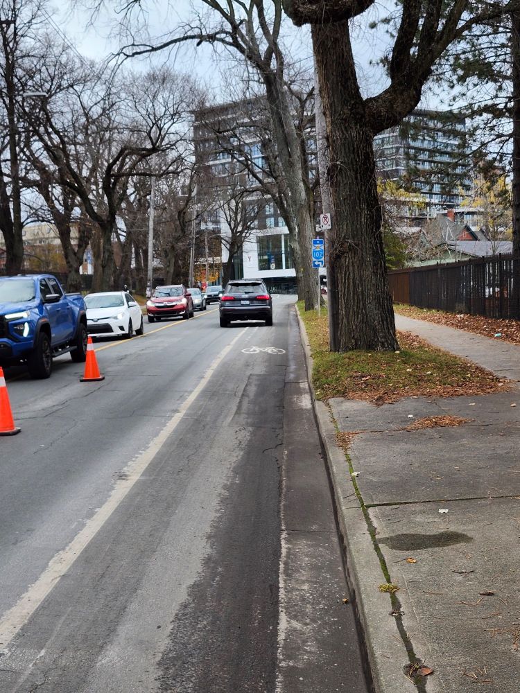 Road with no physical separation between the painted line splitting lanes for bikes and cars.  Car seen in distance driving over the painted line