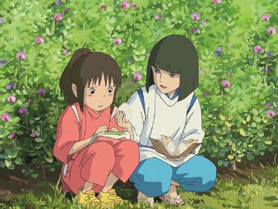 A screenshot from Spirited Away where Chihiro and Haku are squatting low in a flower maze. Haku offers onigiri to Chihiro while she stares at her old clothing folded in her lap.