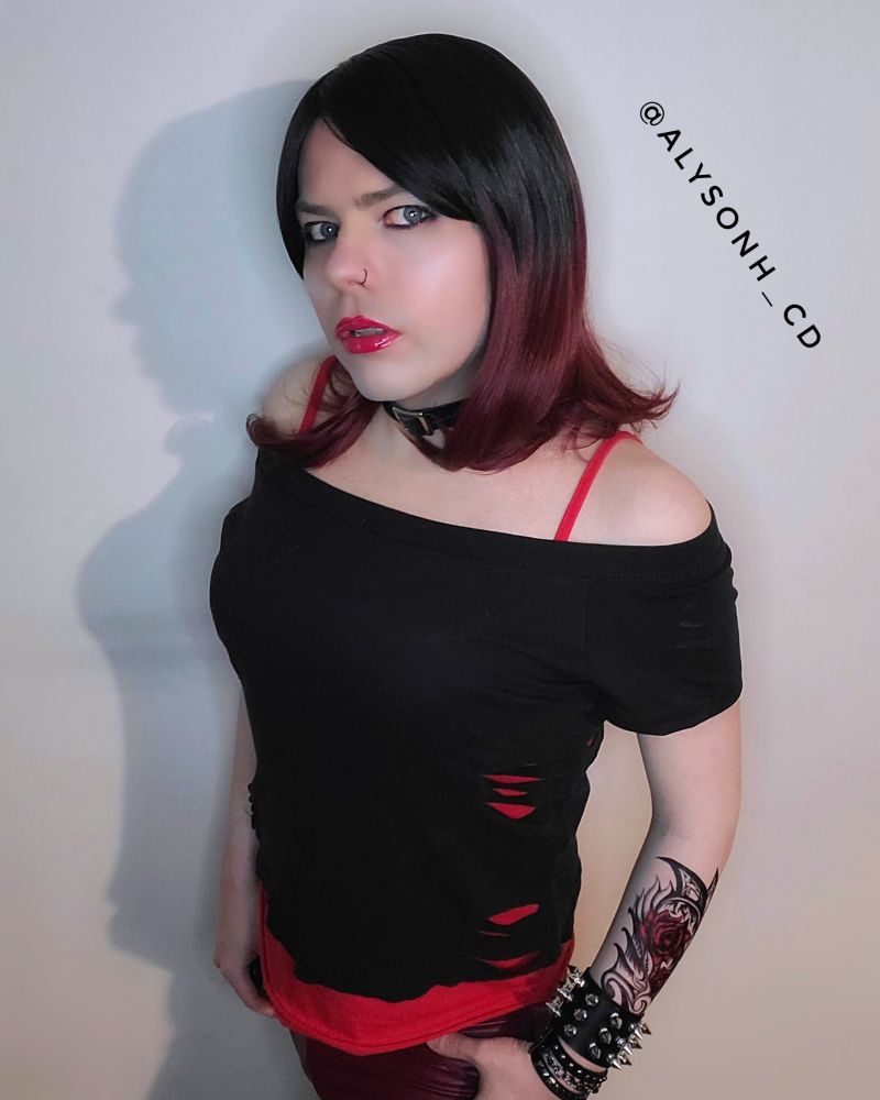 Me dressed as every woman I had a crush on circa 2004.  I'm wearing an off-shoulder black top which is torn in places to show a stroppy red top underneath, with tight dark red leggings. I've got black and red ombre hair, dark eyeliner and glossy red lips. Accessory wise, I'm wearing a small nose ring and several spiked wrist bracers over a fake tattoo. 