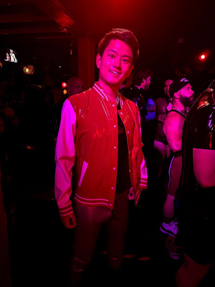 Me in a rubber varsity jacket and rubber pants in a bar in red/purple lighting