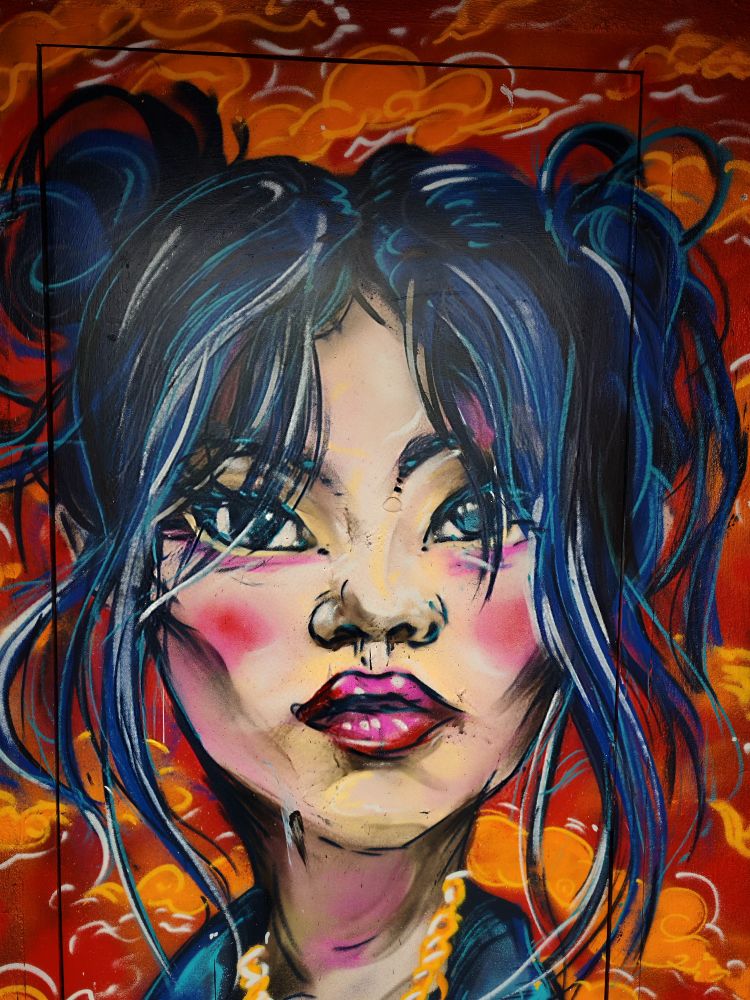 A vibrant graffiti portrait of a woman with blue and black hair, striking eyes, and pink lips against an orange background with swirling patterns.