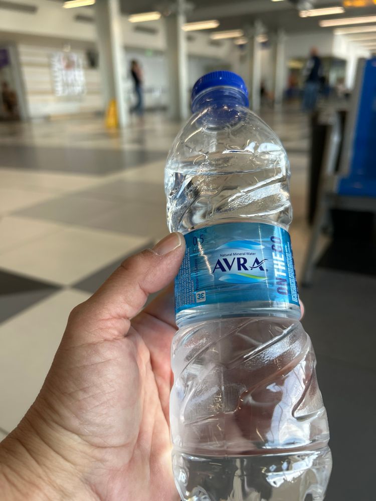 Hand hält Wasserflasche mit griechischer Aufschrift „Aura“