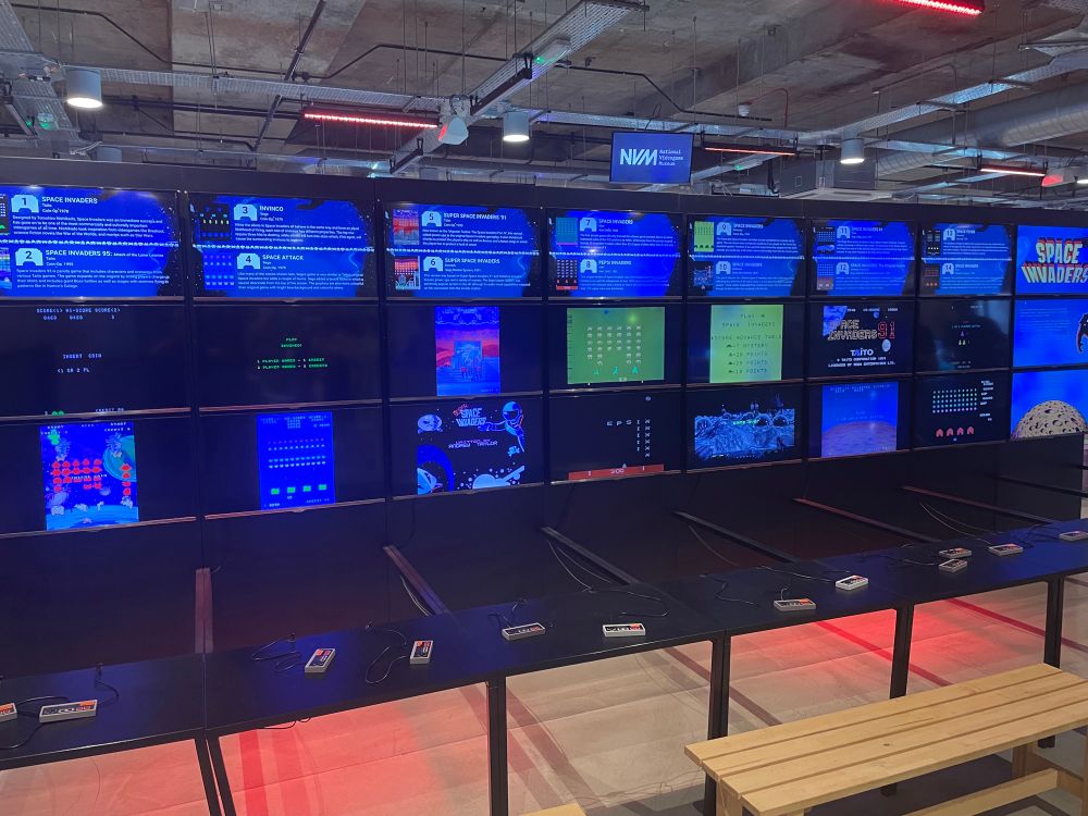 A row of multiple TVs connected to consoles for the Nintendo System. Playing games such as Space Invaders, Super Mario and so on!