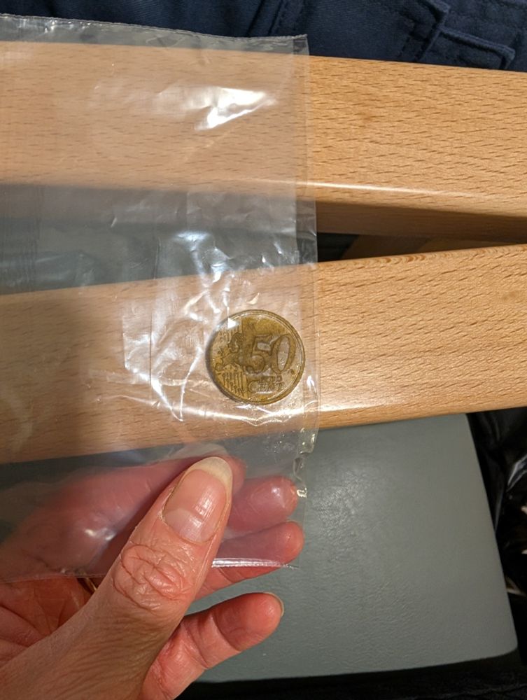 A hand holding a 50 cent coin in a plastic bag.