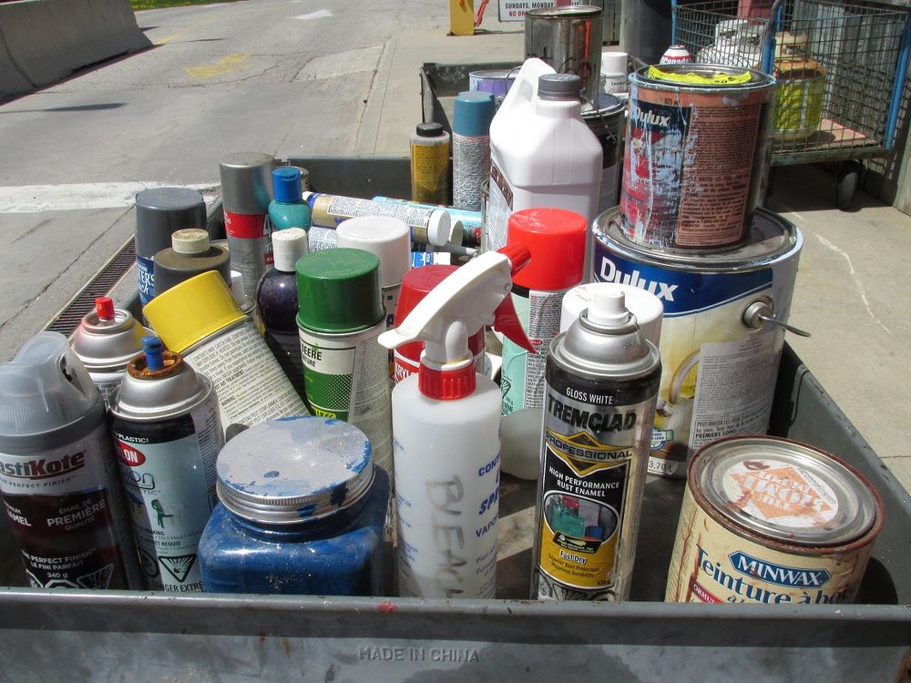 Rolling cart with cans and bottles of various household chemicals, like paint, spray paint and cleaning supplies. 