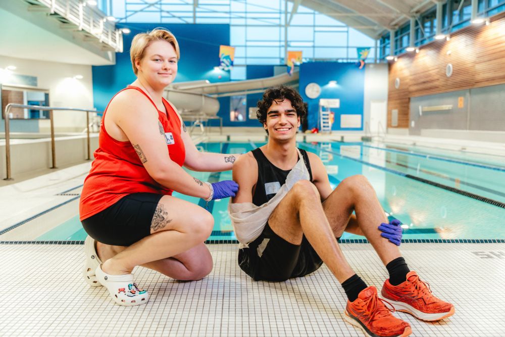 A lifeguard wrapping a persons arms in a sling by a pool in Guelph.