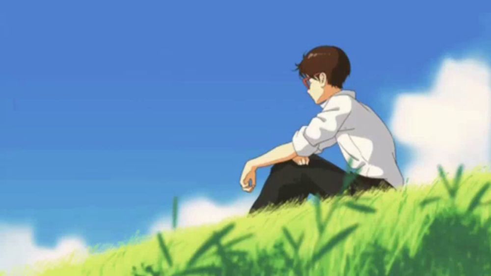 a boy is sitting on a grassy hill with a blue sky behind him