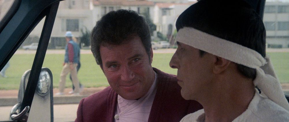 A still from "Star Trek IV: The Voyage Home" -- Kirk and Spock are seated in a 20th century vehicle, bickering about whether or not they're going on a date with Dr. Taylor. Kirk is down to clown, but Spock and his headband aren't so sure.