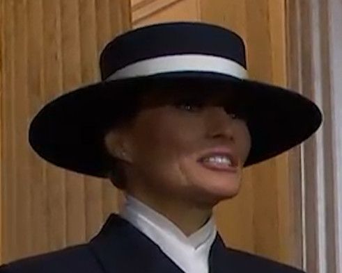 Melania Trump grimacing while wearing a black and white hat.
