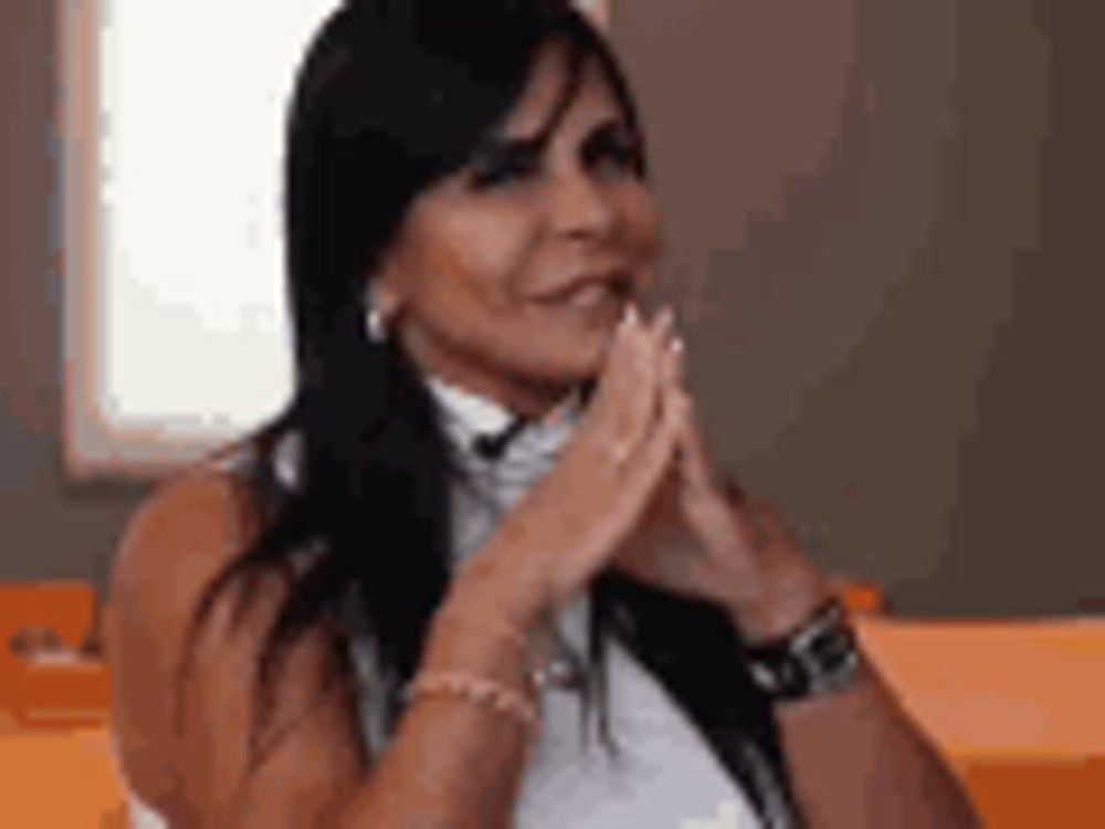 a woman is sitting at a table with her hands folded in prayer .