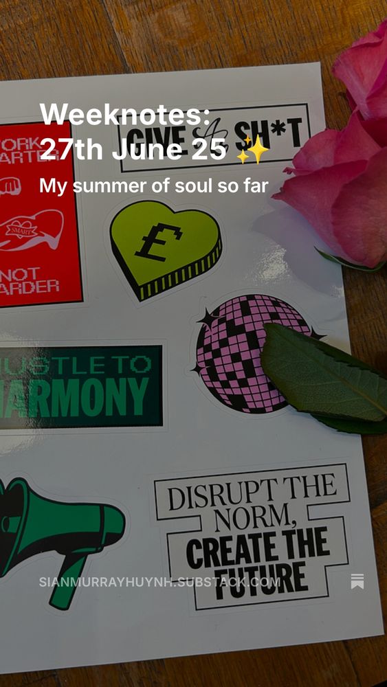 Brightly coloured laptop stickers sit next to two hot pink roses, the stickers include a purple twinkly disco ball, a lime green heart with a pound sign, a dark green heart shaped mega phone speaker, and slogans like "Work smarter not harder", "Give a sh*t", "Hustle to harmony", "Disrupt the norm, create the future"