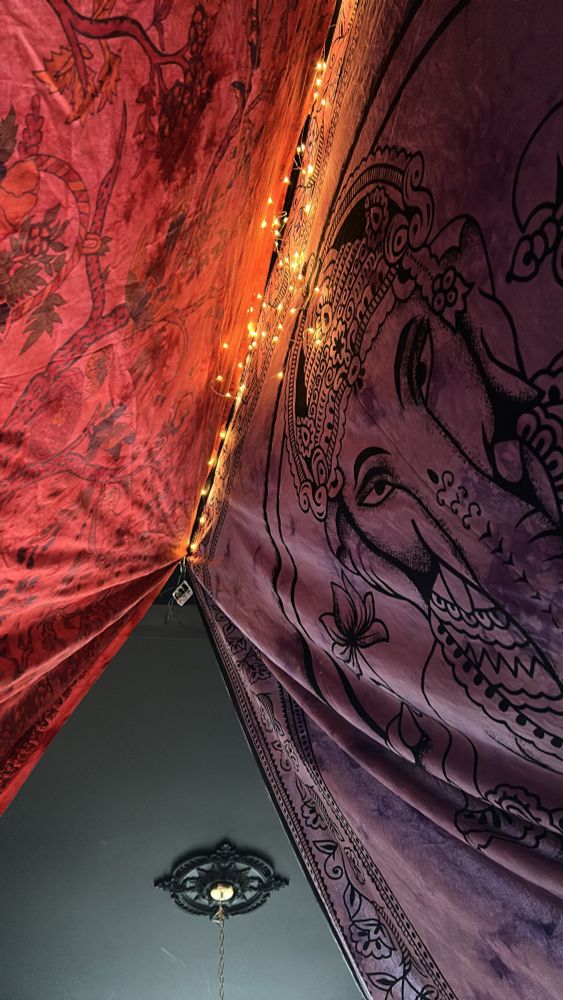 A red and purple tent with Ganesha the Hindu god on it has fairy lights illuminating the inside