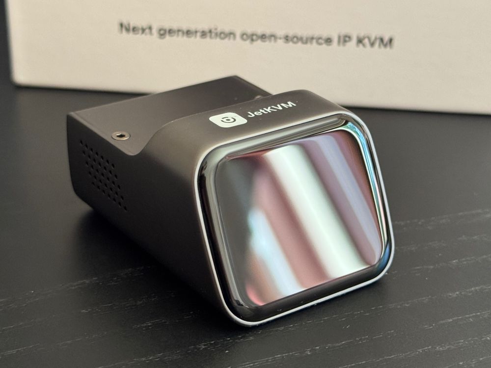 A close up picture of the JetKVM device. It looks like an Apple Watch screen slapped onto a tiny desk device. It’s sleek and polished.

In the background a box reads “Next generation open source IP KVM”