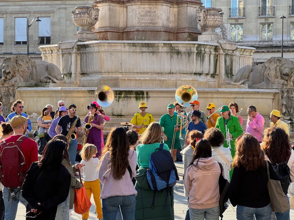 A photo of a fanfare. The band is wearing bright colored clothes and is playing for a crowd in the street
