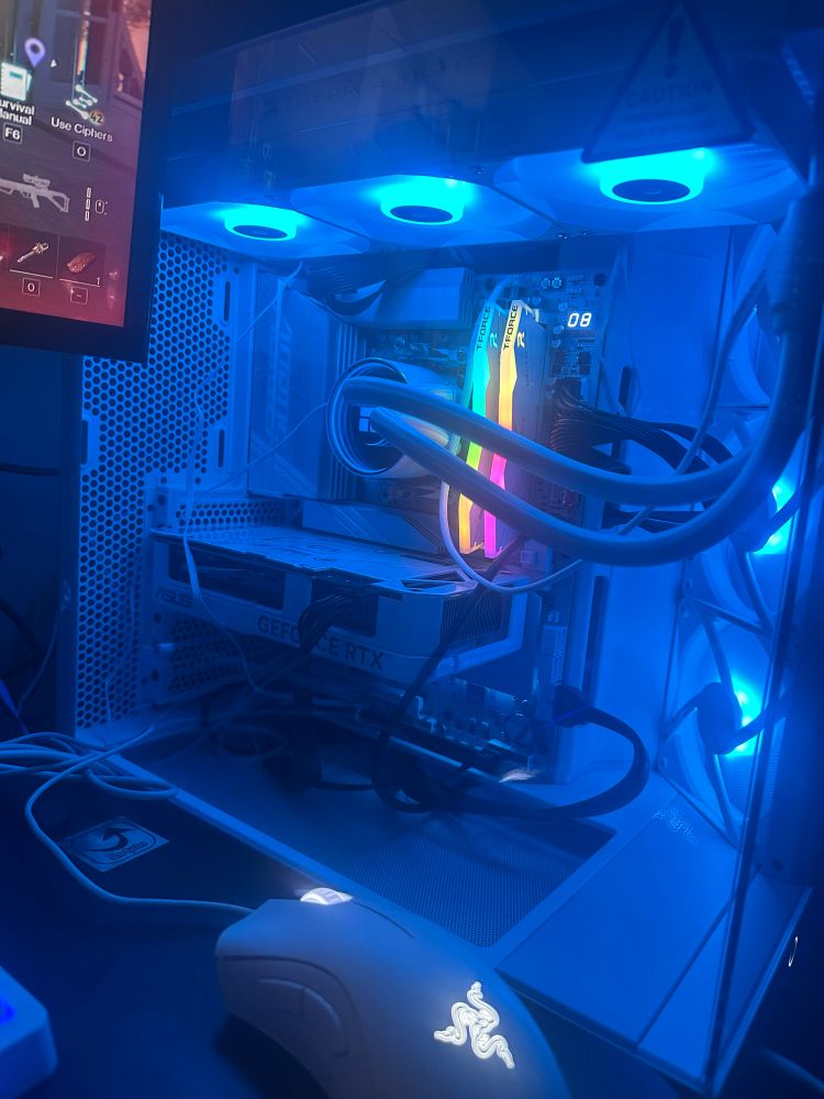 picture of a white gaming pc with black cables. it has blue lighting and the ram lights up in rainbow colors. i also have a white mouse in front of the pc