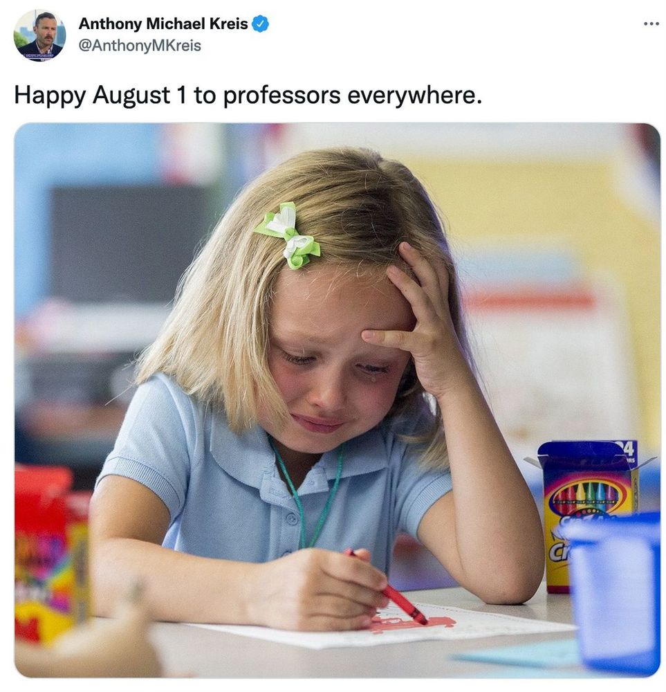 Small child at a desk with a crayon seemingly pretending to draw with a tear in her eye.