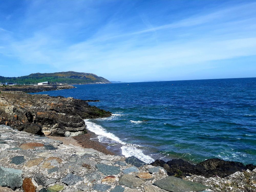 Blue sea with a stony shore in the foreground and cliffs on the horizon 