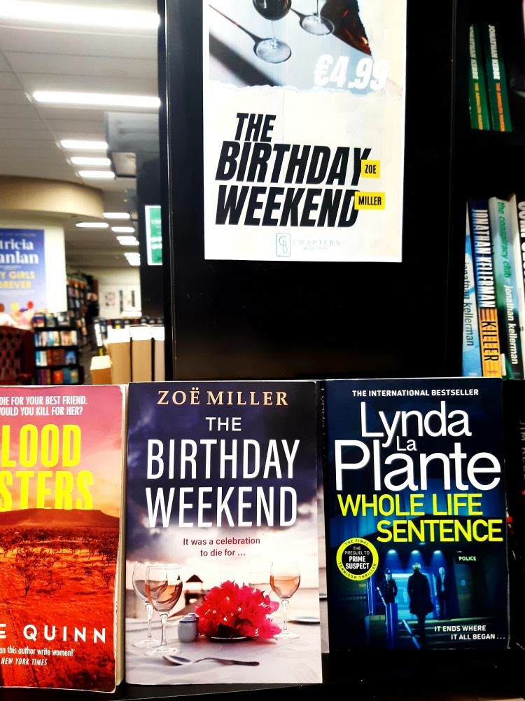 Picture shows books on a bookshelf with The Birthday Weekend in the centre